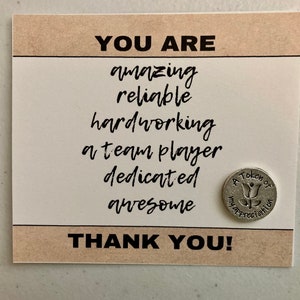 May include: A card with the text "YOU ARE amazing reliable hardworking a team player dedicated awesome THANK YOU!" and a small silver token with the text "A Token of Appreciation" and a stylized flower design.