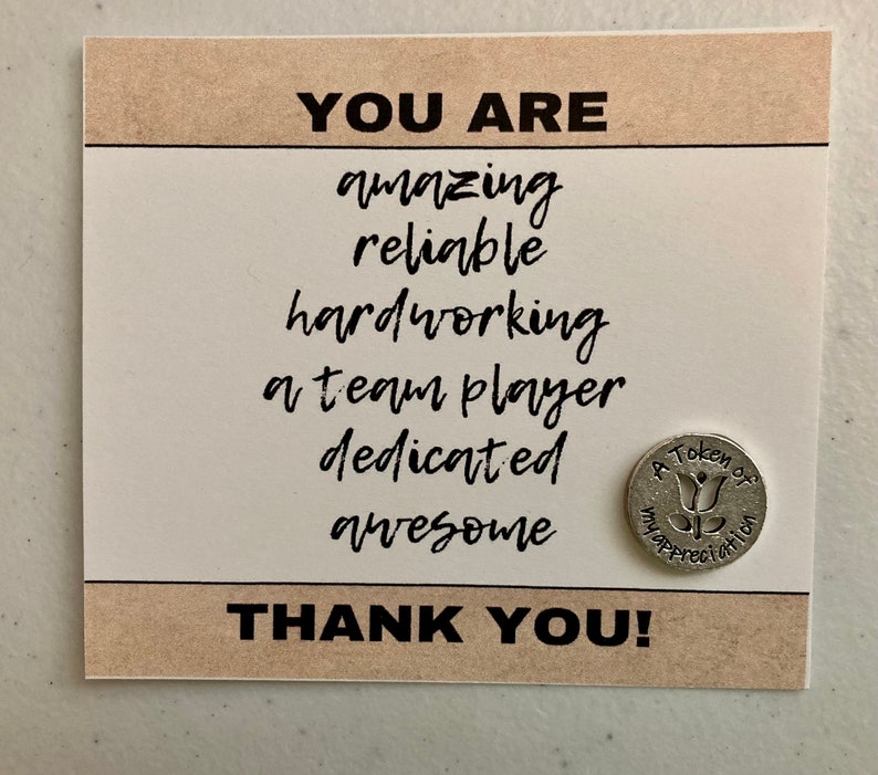 May include: A card with the text "YOU ARE amazing reliable hardworking a team player dedicated awesome THANK YOU!" and a small silver token with the text "A Token of Appreciation" and a stylized flower design.