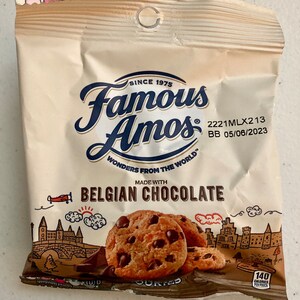 May include: A brown paper bag with a white label featuring the text "Famous Amos" and "Belgian Chocolate". The bag contains chocolate chip cookies and has a drawing of a European city with a castle and a plane.