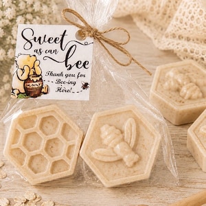 May include: Two hexagonal beige soaps in a clear plastic bag tied with twine. One soap features a honeycomb pattern, the other a bee relief. A white tag attached reads: Sweet as can bee, Thank you for Bee-ing Here!, with a Winnie the Pooh illustration.