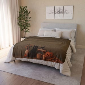 Peut inclure: Une couverture polaire marron avec un motif imprimé représentant un chat noir assis près d'une pile de livres, une citrouille sculptée, une tasse et un vase avec du feuillage d'automne, posée sur un lit avec des oreillers blancs et une tête de lit gris clair.