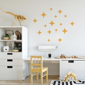 Peut inclure: Un bureau blanc avec une chaise jaune et une étagère blanche sur laquelle se trouve un squelette de dinosaure. Le mur derrière le bureau est décoré d'un motif d'étoiles dorées.