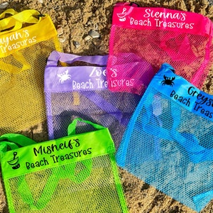 May include: Five colourful mesh bags with adjustable straps. Each bag has a personalised name and the words "Beach Treasures" printed on the front. The bags are on a sandy surface.