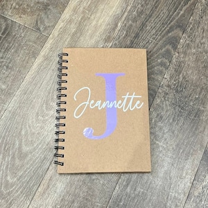 May include: A brown spiral notebook with a purple letter "J" and the name "Jeannette" written in white cursive.