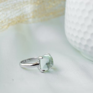 Può includere: Un anello d'argento con una pietra preziosa verde chiaro. L'anello è su uno sfondo bianco.