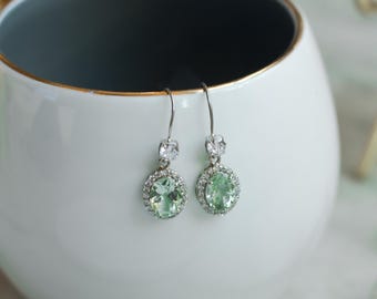 Peut inclure: Une paire de boucles d'oreilles pendantes en argent avec une pierre précieuse verte entourée d'un halo de petites pierres claires.