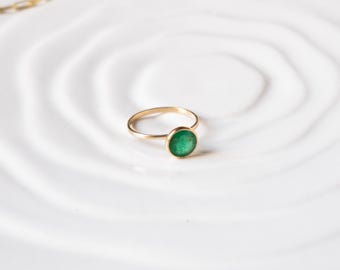 以下が含まれることがあります： ベゼルセッティングにセットされた緑色の宝石が付いた金の指輪。指輪は白い背景の上に置かれています。