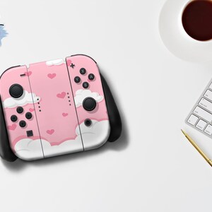 Op de afbeelding: Een roze Nintendo Switch-console met een wolk- en hartpatroon. De console heeft zwarte joysticks en knoppen. Het Sweet Wild Designs-logo is linksboven zichtbaar.