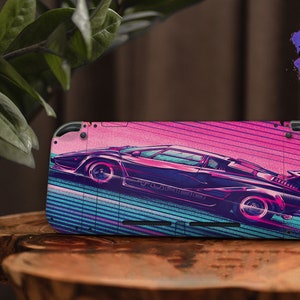 Puede incluir: Una piel para Nintendo Switch de color rosa, azul y morado con una ilustración retro de un coche deportivo negro. El coche circula por una carretera con rayas azules y moradas. La piel tiene el texto "Sweet Wild Designs" en la esquina superior derecha.
