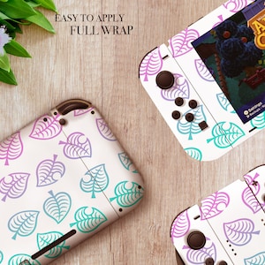 May include: A white Nintendo Switch console and two controllers with a full wrap skin featuring a pattern of pink and blue leaf designs. The text "Animal Crossing" is visible on the console screen.