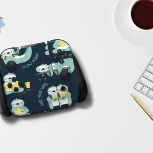 Pu&ograve; includere: Una skin per console Nintendo Switch blu scuro con un motivo ripetitivo di bradipi che tengono tazze e il testo "Slow Down" e "Take Your Time".