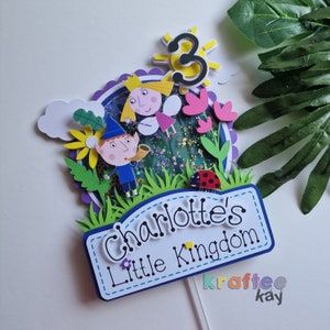 May include: A colorful cake topper featuring characters from the children's show 'Ben & Holly's Little Kingdom'. The topper includes Ben, Holly, a ladybug, flowers, and a sun with the number 3. The topper also includes a sign that says 'Charlotte's Little Kingdom'.