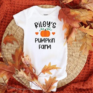 May include: White baby onesie with the text "Riley's Pumpkin Farm" and a small orange pumpkin with green stem and three red hearts.