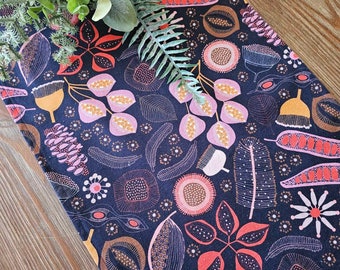 May include: A dark blue table runner with a repeating pattern of pink, orange, and brown stylized flowers and leaves. The pattern is outlined in white.