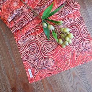 May include: Red and brown table runner with a repeating pattern of circles and lines. The runner is folded in half and has a tag that says "Dream Weavers".
