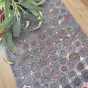 May include: A rectangular table runner featuring a dense dot art pattern of overlapping circles in shades of black, dark blue, purple, pink, and yellow. The fabric surface is covered in intricate, small dots that create a textured visual effect.