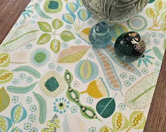 May include: A white table runner with a green and yellow floral pattern. The runner features a variety of leaves, flowers, and seeds. The runner is perfect for adding a touch of nature to your dining table.
