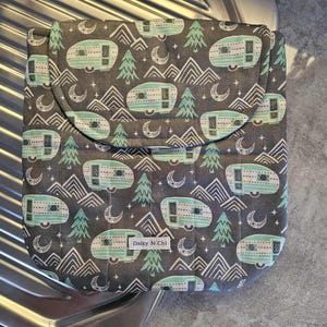 May include: A gray fabric case with a flap closure, patterned with teal and white camper trailers, trees, mountains, and crescent moons. The case has a label that reads "Daisy N Chi".