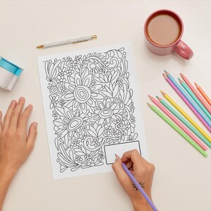 Pu&ograve; includere: Una persona sta colorando un disegno floreale in bianco e nero con una matita viola. Il disegno &egrave; su un foglio di carta bianco. Ci sono una variet&agrave; di matite colorate e una tazza di caff&egrave; sul tavolo.
