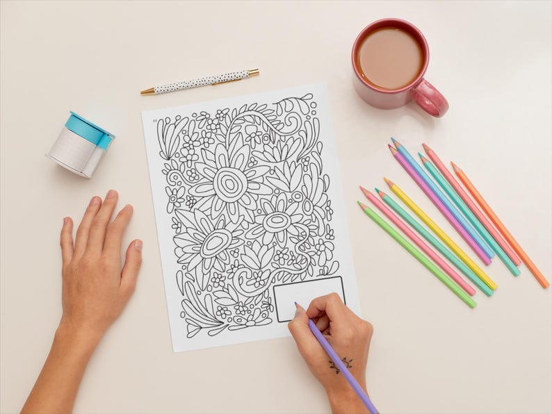Pu&ograve; includere: Una persona sta colorando un disegno floreale in bianco e nero con una matita viola. Il disegno &egrave; su un foglio di carta bianco. Ci sono una variet&agrave; di matite colorate e una tazza di caff&egrave; sul tavolo.