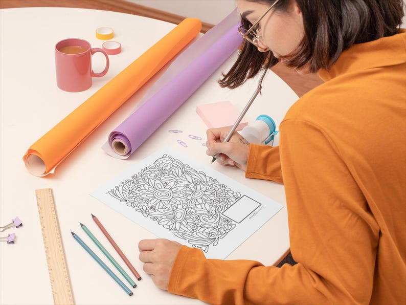 Pu&ograve; includere: Una persona sta colorando un disegno floreale dettagliato in bianco e nero su un foglio di carta con una matita. La persona &egrave; seduta a un tavolo con un righello, matite e due rotoli di carta da regalo.