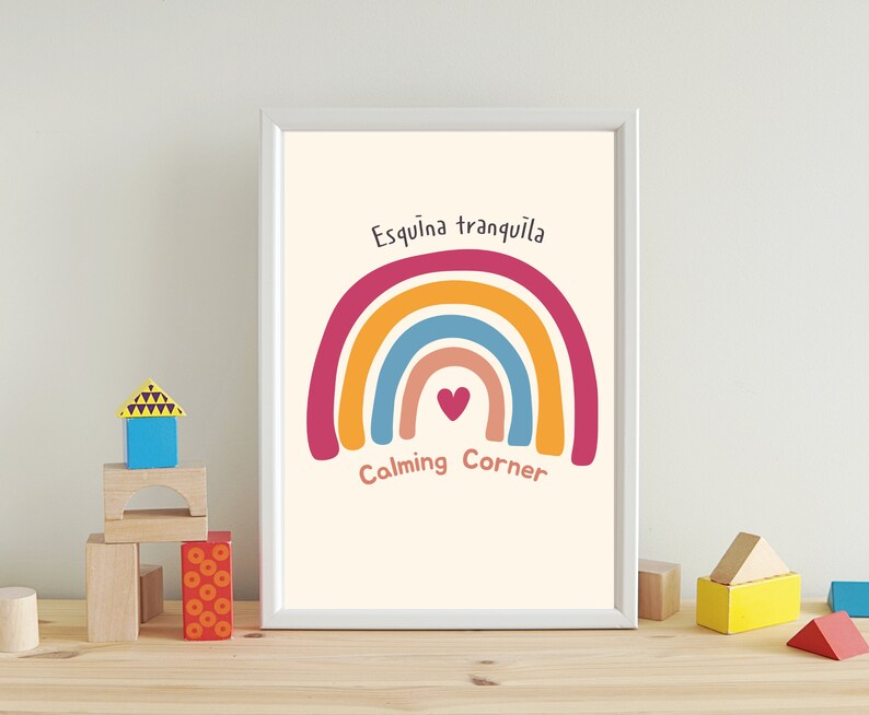 May include: A white framed print with a rainbow design and the text "Esquina tranquila" and "Calming Corner". The rainbow is made up of red, orange, yellow, blue, and pink. There is a small heart in the center of the rainbow.