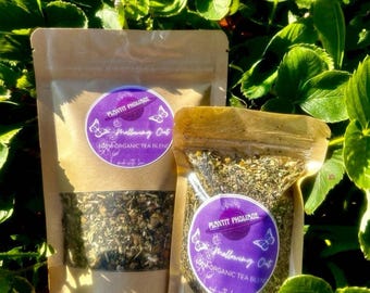 May include: Two brown paper bags filled with loose leaf tea. The bags have purple labels with the text "PLANTIT PHOLIAGE" and "Mellowing Out" with a butterfly graphic. The text "100% ORGANIC TEA BLEND" is also on the label.