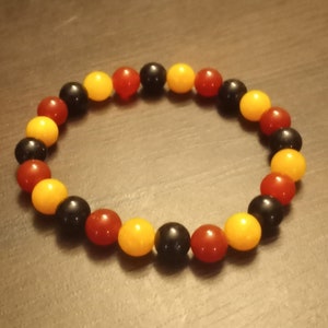 May include: A bracelet made of black, red and yellow beads. The beads are arranged in a repeating pattern.