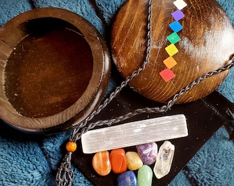 May include: A wooden box with a lid, a white crystal, and seven chakra stones in a pouch. The stones are red, orange, yellow, green, blue, indigo, and violet. The pouch is black with a cord and a wooden bead.