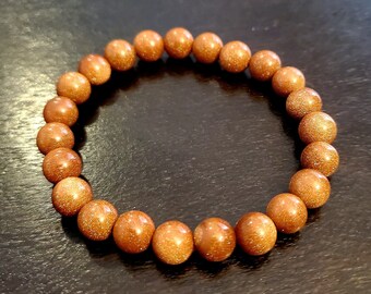 May include: A brown beaded bracelet made of natural stone. The beads are round and have a speckled texture.
