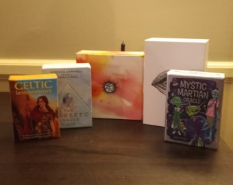 Può includere: Una collezione di cinque mazzi di carte da tarocchi e oracoli. I mazzi sono di dimensioni diverse e hanno vari disegni. I mazzi includono Celtic Lenormand, The Starseed Oracle, Mystic Martian Oracle e altri due mazzi con disegni astratti.