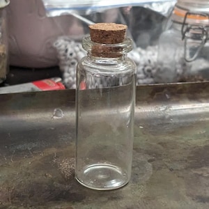 May include: A clear glass bottle with a cork stopper. The bottle is empty and has a cylindrical shape.