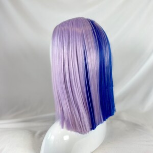 May include: A short, straight wig with a lavender and blue color split. The wig is styled with a side part and is worn on a white mannequin head.
