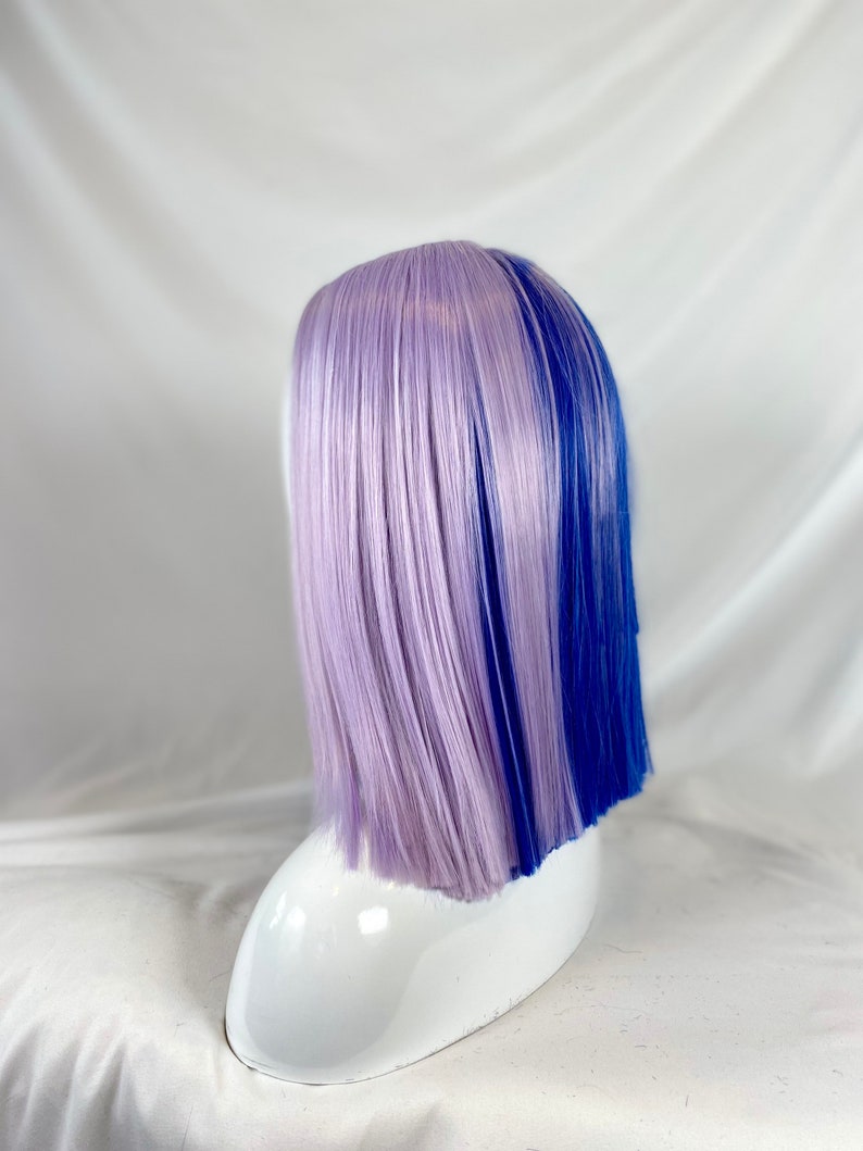 May include: A short, straight wig with a lavender and blue color split. The wig is styled with a side part and is worn on a white mannequin head.