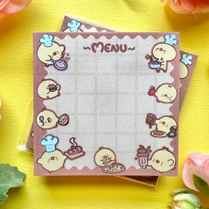May include: A brown and white menu notepad with a grid pattern and illustrations of cute cartoon chicks. The notepad has the word "MENU" written on it.