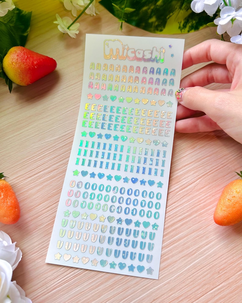 May include: A sheet of holographic stickers with the word "Micashi" in rainbow lettering. The stickers include the alphabet, numbers, hearts, stars, and other shapes in various colors.