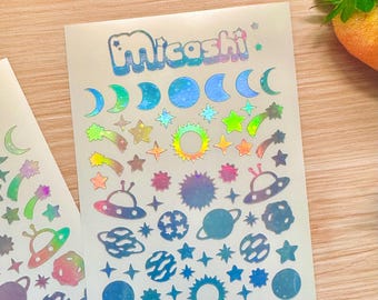 May include: Holographic stickers featuring celestial and space-themed designs. The stickers include moons, stars, planets, shooting stars, suns, and UFOs. The word "Micoshi" is printed at the top of the sticker sheet in a bubble font.