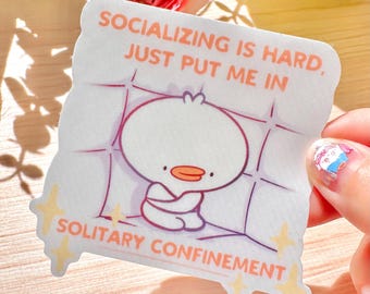 Puede incluir: Una pegatina blanca con una ilustración de un pato de dibujos animados. La pegatina tiene el texto "SOCIALIZING IS HARD, JUST PUT ME IN SOLITARY CONFINEMENT" en naranja y morado. El pato está sentado con los brazos cruzados.