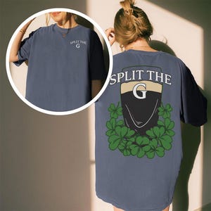 May include: A navy blue t-shirt with the text "SPLIT THE G" on the front and back. The back features a graphic of a shield with a "G" inside, surrounded by shamrocks. The shirt is a comfortable, casual style.