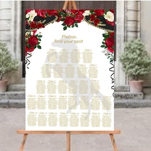 May include: A wedding seating chart displayed on an easel. The white sign features a decorative floral arch with red roses and black sombreros. The text "Please, find your seat" is at the top. The chart lists guest names by table number.