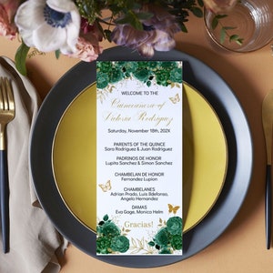 May include: A Quinceañera programme with a green and gold floral design. The programme lists the names of the parents, godparents, and attendants of the Quinceañera, Victoria Rodriguez. The programme is set on a table with a gold and black plate and a beige napkin.