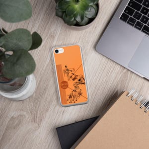 Puede incluir: Una funda de teléfono transparente con un fondo naranja y una ilustración en blanco y negro de atletas practicando deportes. La ilustración incluye el texto "Red Skins" y "Springfield, Mass."
