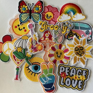 May include: A collection of colorful embroidered patches with a retro, hippie theme. Designs include a butterfly, flowers, a rainbow, a peace sign, a mushroom, a guitar, and the words "Peace Love" and "Groovy".