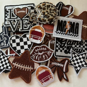 May include: A collection of embroidered patches with a football theme. Designs include footballs, helmets, hearts, stars, lips, and the words "LOVE", "MAMA", and "Game Day". Colors include brown, white, black, and leopard print.