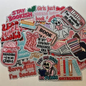 May include: A collection of embroidered patches with book-themed designs. The patches feature phrases like "Stay Bookish," "Read More Books," and "Reading is My Jam." Other designs include cowboy boots, a ghost reading a book, and a stack of books. The color palette includes pink, red, and white.