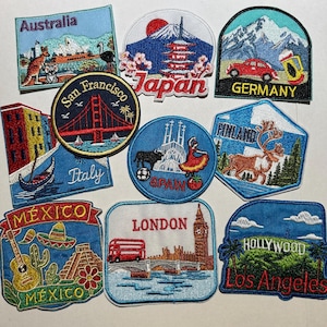 May include: A collection of embroidered travel patches featuring iconic landmarks and symbols from various countries and cities. Patches include Australia, Japan, Germany, Italy, Spain, Finland, Mexico, London, and Hollywood, Los Angeles. Each patch has a unique design and color scheme.