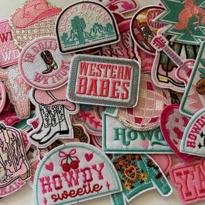 May include: A collection of embroidered patches in shades of pink, white, and turquoise. The patches feature Western-themed designs, including cowboy boots, a cactus, a disco ball, and the text "Western Babes" and "Howdy Sweetie".