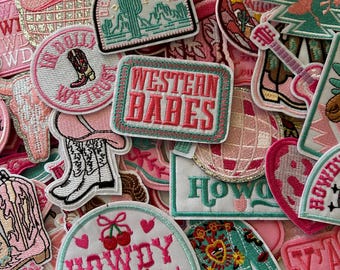 May include: A collection of embroidered patches in shades of pink, white, and turquoise. The patches feature Western-themed designs, including cowboy boots, a cactus, a disco ball, and the text "Western Babes" and "Howdy Sweetie".