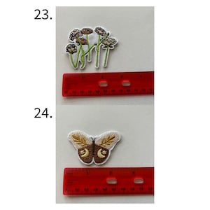 May include: Two embroidered patches. The top patch features a cluster of flowers with green stems and leaves. The bottom patch is a butterfly with tan and brown wings and a crescent moon design. A red ruler is next to each patch.