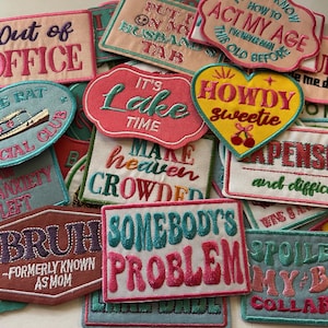 May include: A collection of embroidered patches in various shapes and colors. The patches feature phrases like "Out of Office," "Howdy Sweetie," and "Somebody's Problem." The patches have a retro, vintage aesthetic.
